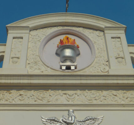 Architectural details of a building featuring intricate carvings and a flame motif against a clear blue sky.