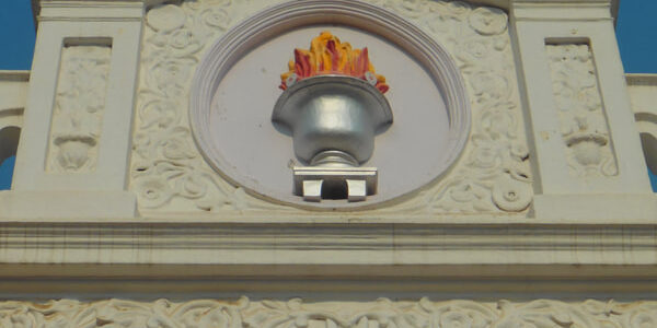 Architectural details of a building featuring intricate carvings and a flame motif against a clear blue sky.