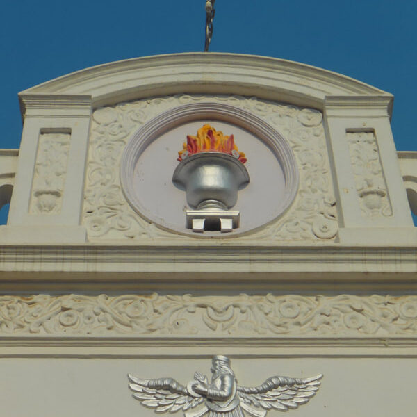Architectural details of a building featuring intricate carvings and a flame motif against a clear blue sky.