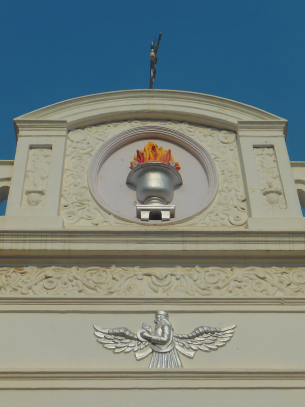 Architectural details of a building featuring intricate carvings and a flame motif against a clear blue sky.